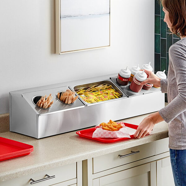 A woman standing at a counter with a tray of food and a container of condiments. One of the squeeze bottles is in the foreground.