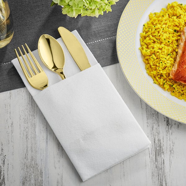 A white linen pocket fold napkin with gold cutlery on a plate of rice and meat.