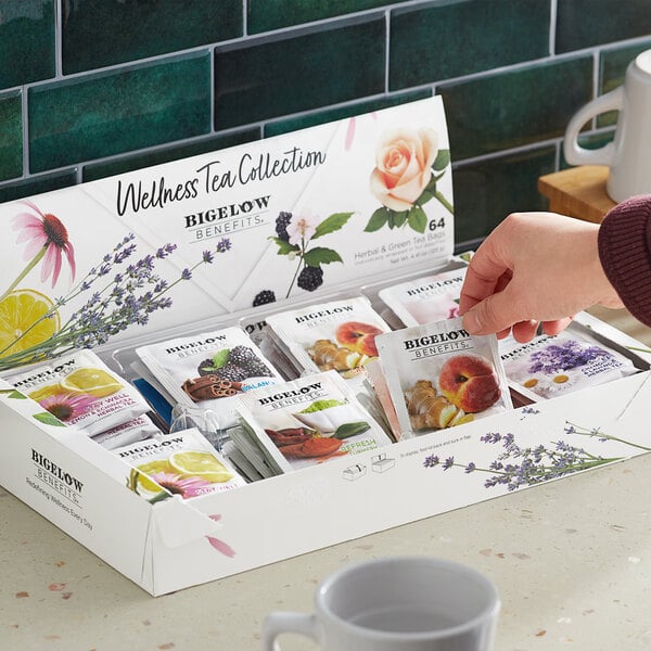 A woman's hand taking a Bigelow Benefits Wellness Tea bag packet from a box.