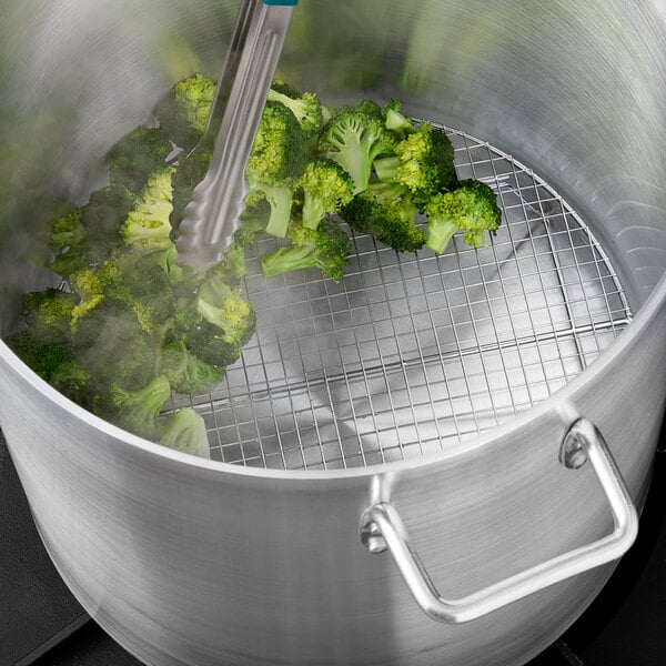 A round chrome steamer rack holding steamed broccoli over a pot.