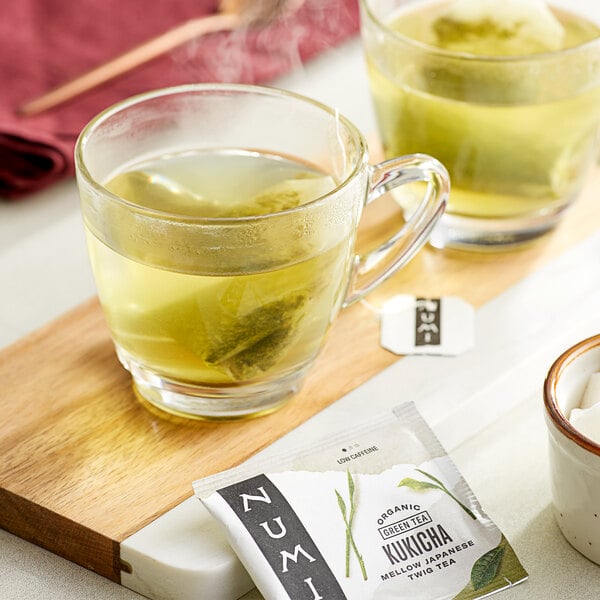 A pair of glass cups of Numi Kukicha tea with tea bags in them.