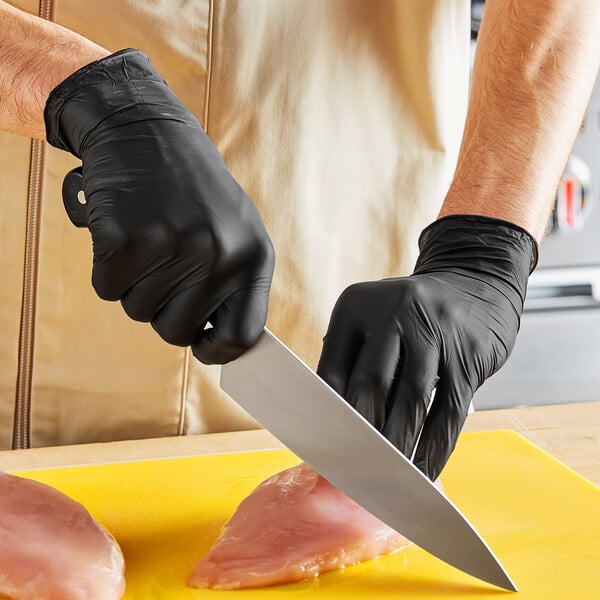 A person wearing black Noble Nitrile gloves cutting meat on a cutting board.