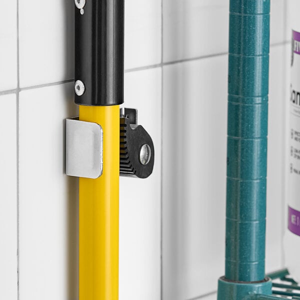 A yellow American Specialties, Inc. mop holder attached to a white tile wall with a yellow and black mop in it.