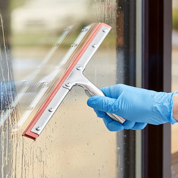 A hand in a blue glove using a Lavex window squeegee to clean a window.