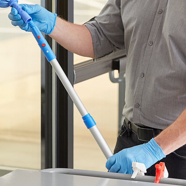 A man using a Lavex telescopic pole with a mop adapter to clean a table.