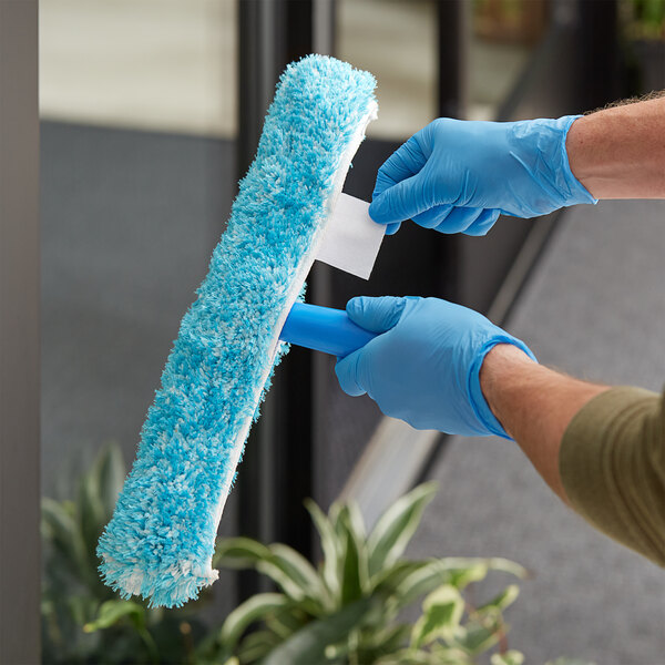 A person wearing blue gloves using a Lavex blue window cleaning sleeve to clean a window.