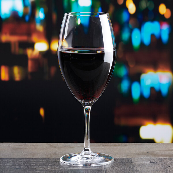 A clear Lucaris Serene 16 oz. cabernet wine glass filled with red wine, placed on a wooden surface.