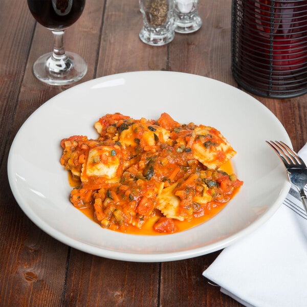 A Tuxton Eggshell China pasta bowl filled with pasta and sauce on a table.