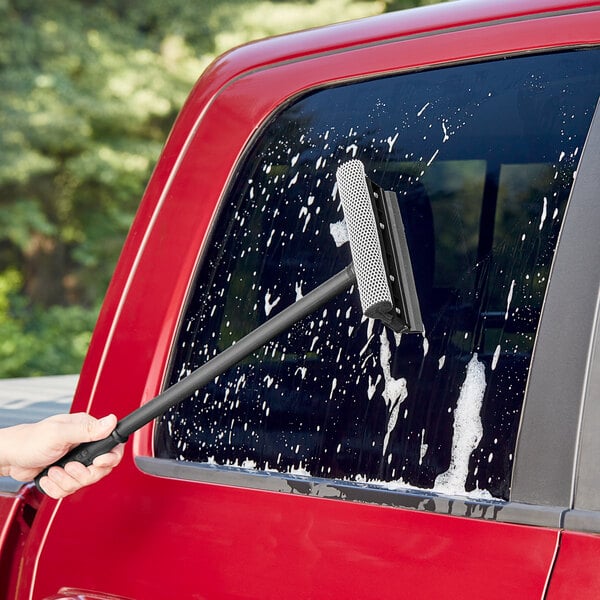 A hand using a Lavex window squeegee to clean a car window.