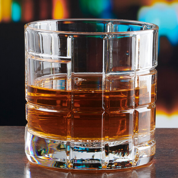 A clear, textured rocks glass partially filled with a brown liquid, likely whiskey or another spirit.
