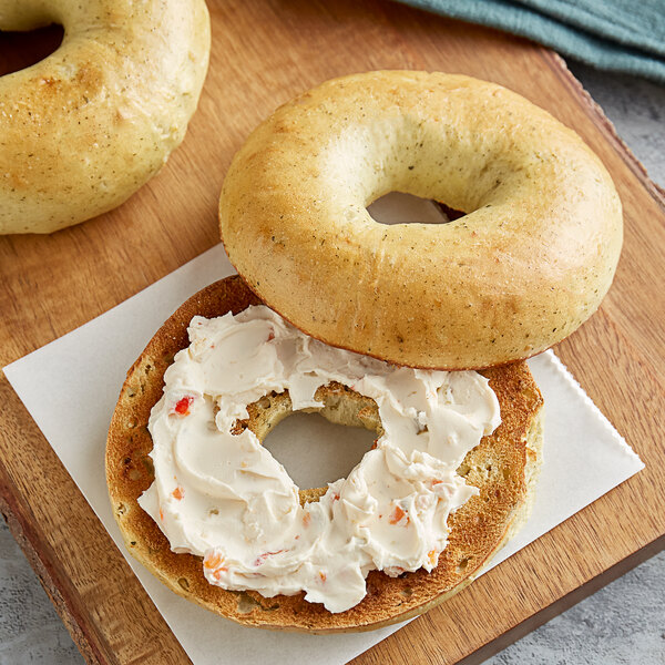 A frozen Original Bagel spinach bagel on a wooden board with cream cheese.