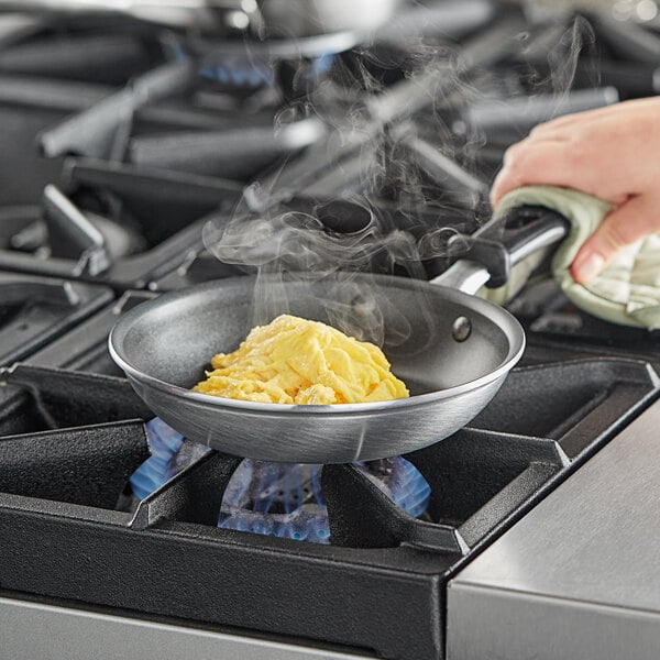A person using a Vollrath Wear-Ever aluminum non-stick fry pan to cook eggs on a stove.