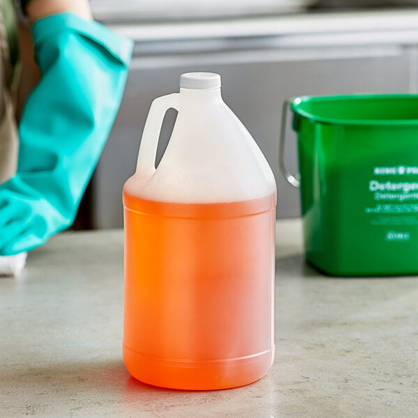 A person wearing green gloves holding a translucent jug with white lid filled with liquid.