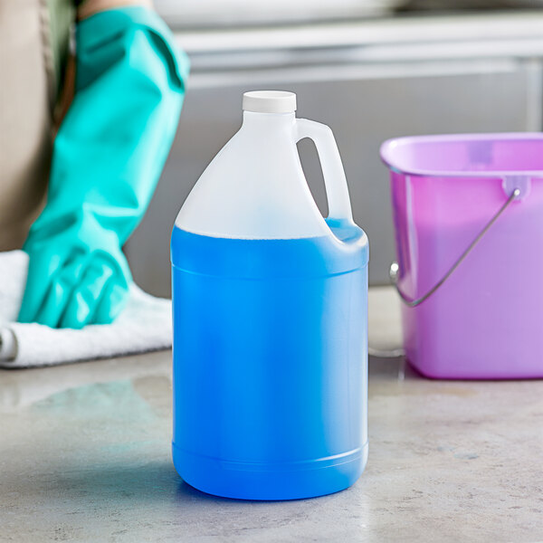A translucent HDPE jug filled with blue cleaning liquid with a white cap next to a blue bucket and gloves.