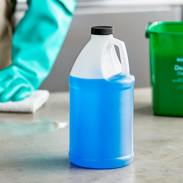 A gloved hand holding a translucent HDPE jug of blue liquid with a black cap.