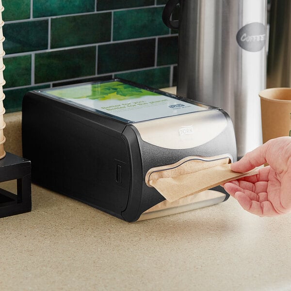 A black Tork Xpressnap countertop napkin dispenser on a counter.