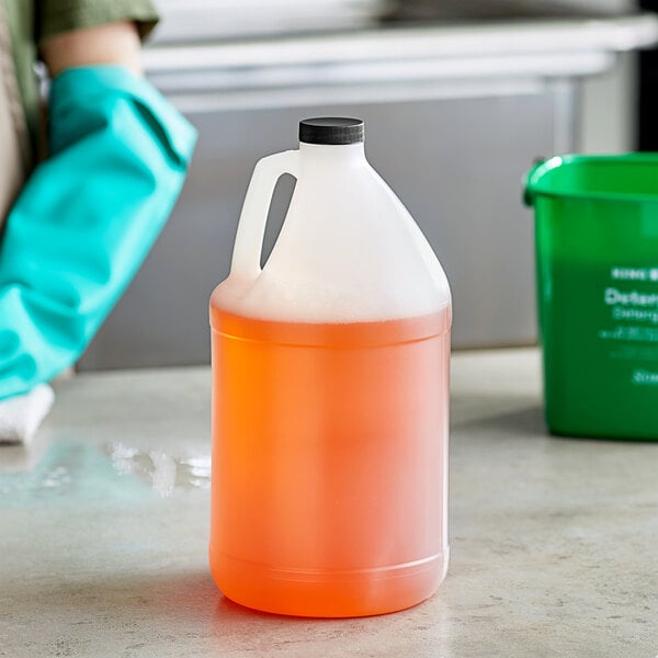A woman in green gloves holding a translucent HDPE jug of liquid with a black cap and handle.
