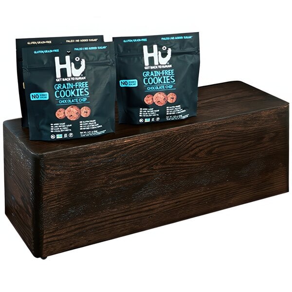 A group of bags of Hugo's chocolate chip cookies on a rectangular oak display riser.