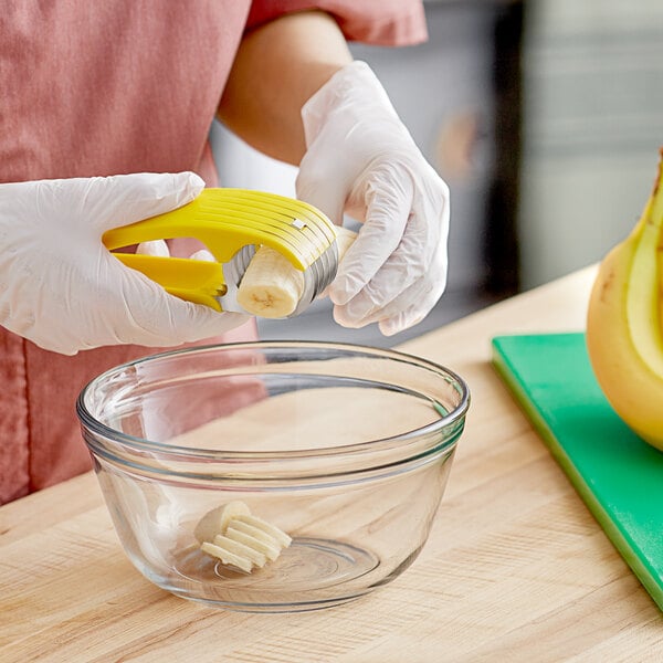 A person's hand uses a Taylor Bananza banana slicer to peel a banana.
