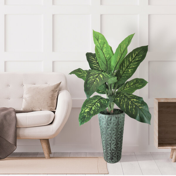 A 48" artificial Dieffenbachia plant in a copper washed metal planter on a wood surface next to a white couch.