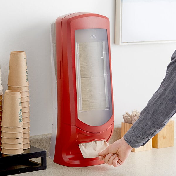 A person refilling a red Tork Xpressnap interfold napkin dispenser.