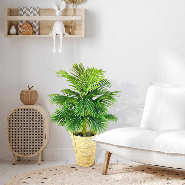 An artificial Areca Palm tree in a wooden basket with handles next to a white chair.
