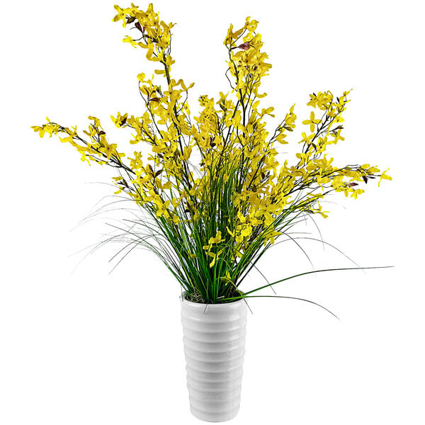 A white cylindrical vase with yellow artificial forsythia flowers.