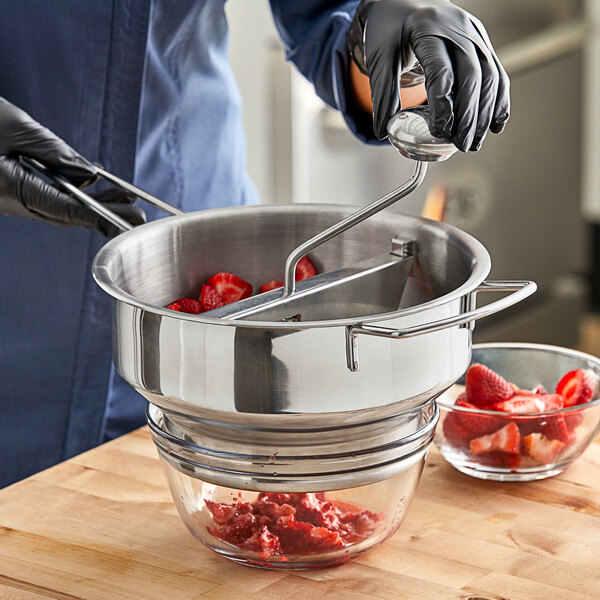 A person in a blue uniform using a Choice Prep stainless steel rotary food mill to process strawberries.