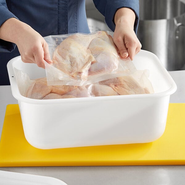 A person putting a bag of chicken in a white Choice plastic food storage container.