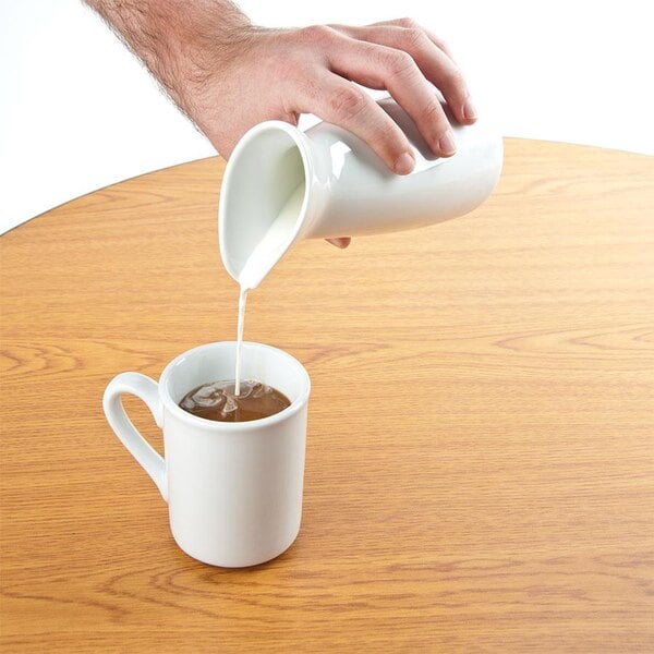 A person pouring milk into a white cup of coffee.