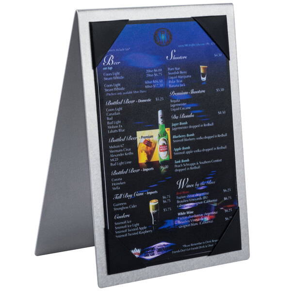 A Menu Solutions brushed aluminum menu tent with picture corners on a table with a silver metal frame holding a menu.