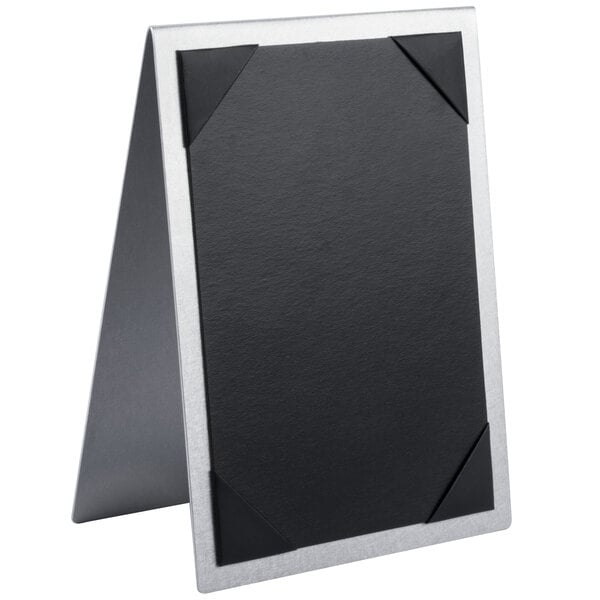 A black and silver Menu Solutions Alumitique table tent with picture corners holding a black and white menu on a table.
