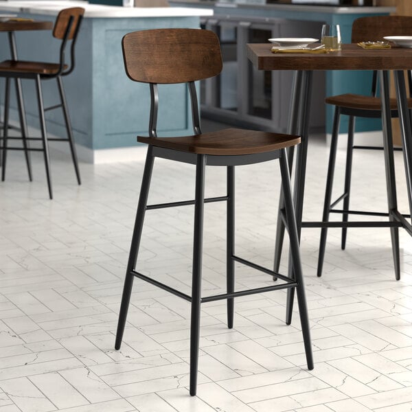 A Lancaster Table & Seating black barstool with wood seat and backrest on a table next to a counter.