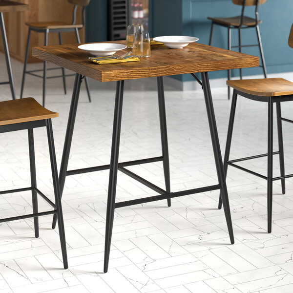 A Lancaster Table & Seating black bar height table base with a wooden table and chairs.