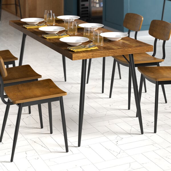 A Lancaster Table & Seating butcher block table with plates and glasses on it and chairs with wood seats and black legs.