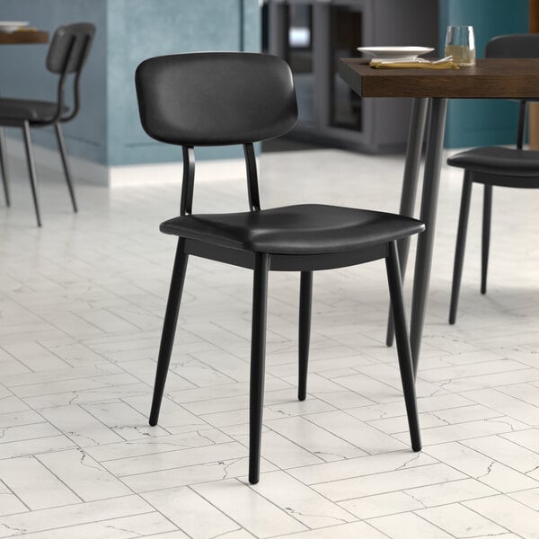 A Lancaster Table & Seating black chair with black vinyl padded seat and backrest on a table in a restaurant dining area.