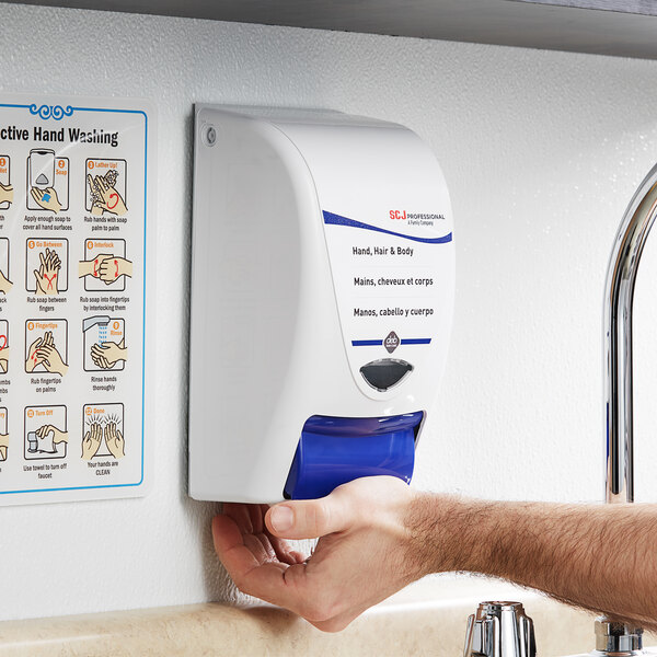 A white and blue SC Johnson Professional hand, hair, and body wash dispenser on a wall.