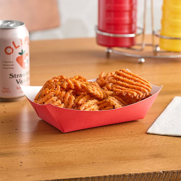 A red paper food tray with potato chips and strawberries on a table.