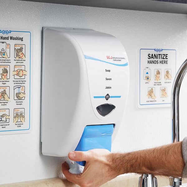 A person using a SC Johnson Professional foaming hand soap dispenser on a wall.