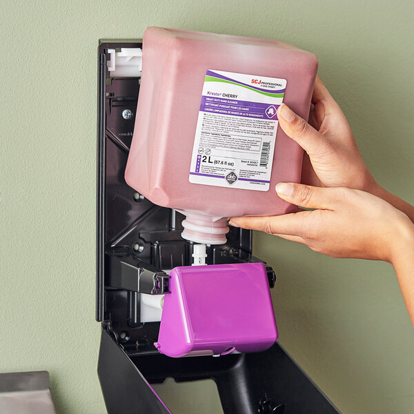 A person's hand holding a pink plastic container of SC Johnson Professional Kresto Cherry Heavy-Duty Hand Soap.