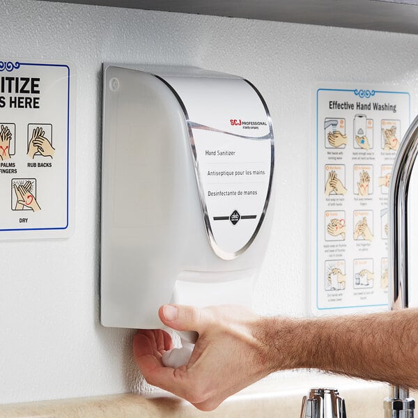 A person using a SC Johnson Professional white and gray foaming hand sanitizer dispenser.