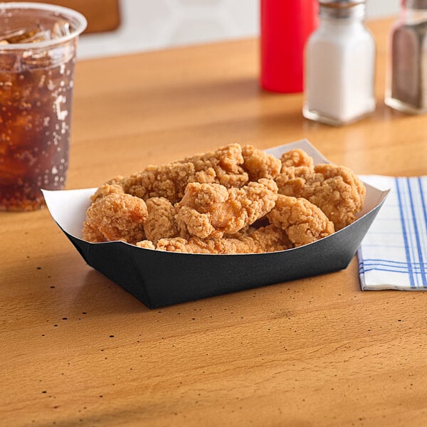 A #200 solid black paper food tray of fried chicken on a table.