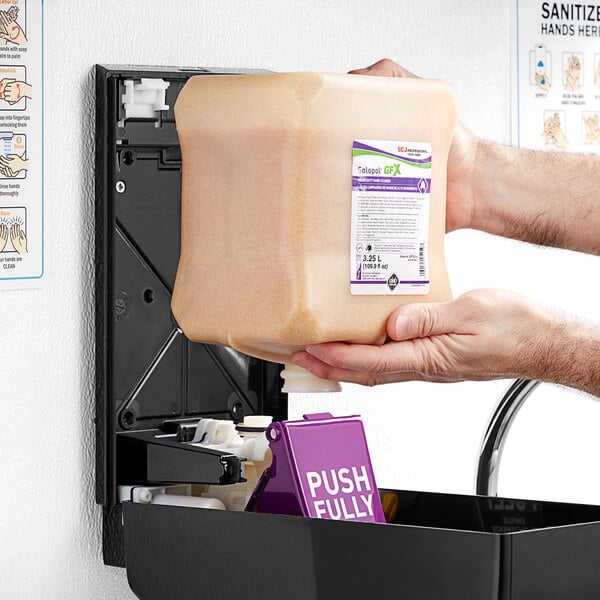 A person putting a SC Johnson Professional Solopol GFX heavy-duty foaming hand soap refill into a dispenser.