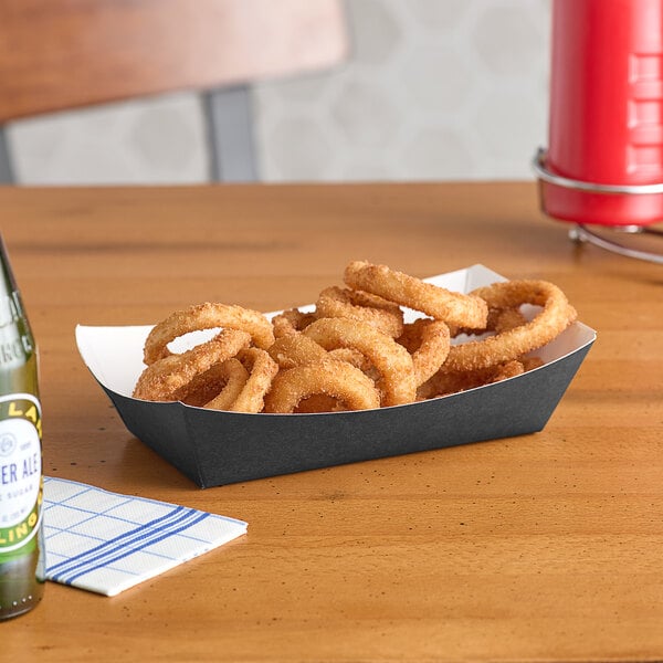 A solid black paper food tray with fried onion rings on a table.