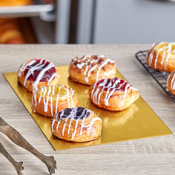 A table with a group of pastries on rectangular gold and silver Enjay dessert boards.