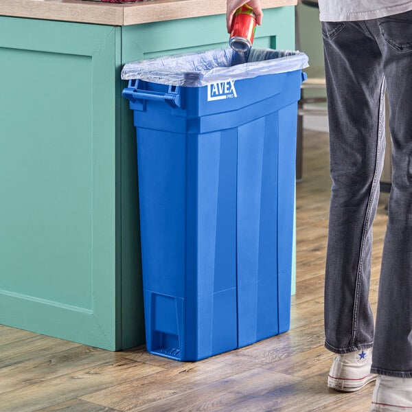 A man in a pair of jeans standing next to a Lavex Pro blue slim rectangular trash can.