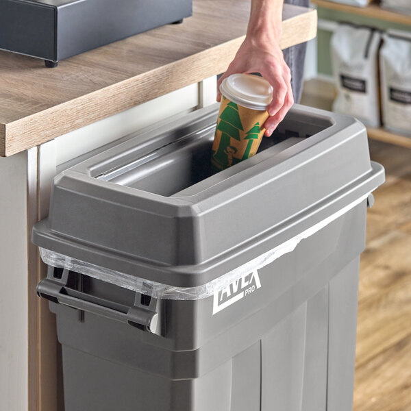 A person putting a coffee cup into a Lavex Pro slim rectangular trash can.