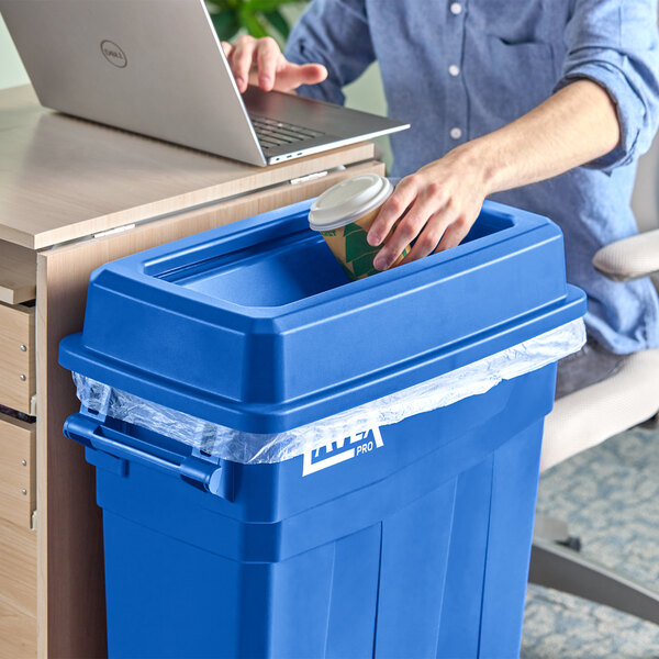 A hand puts a coffee cup in a blue Lavex Pro slim rectangular trash can.