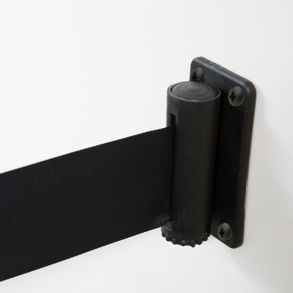 A black Aarco wall mounted stanchion belt clip attached to a wall.