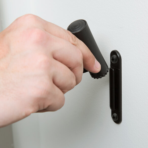 A hand holding a black Aarco wall mounted stanchion belt clip cylinder.